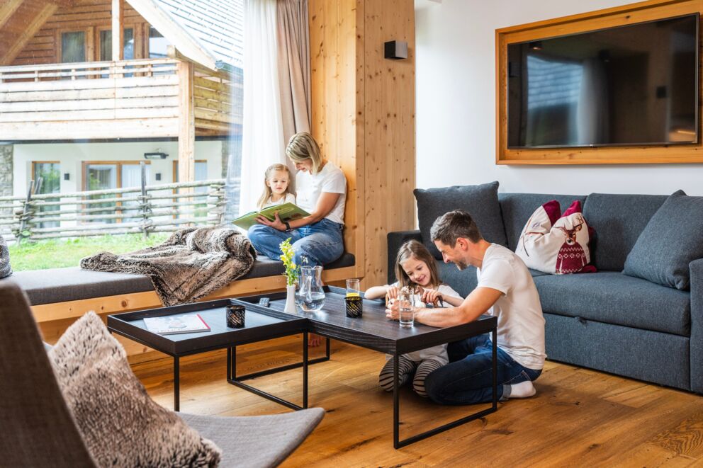 Familie genießt gemeinsame Zeit in gemütlichem Chalet-Wohnzimmer mit Holzelementen.