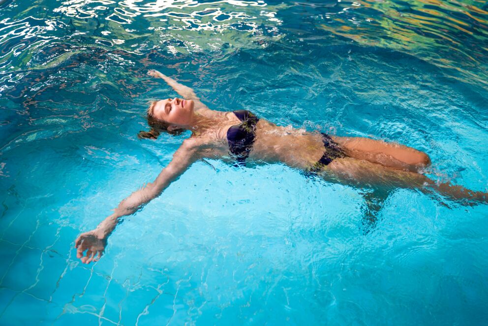 Donna in bikini blu che galleggia rilassata in una piscina trasparente.