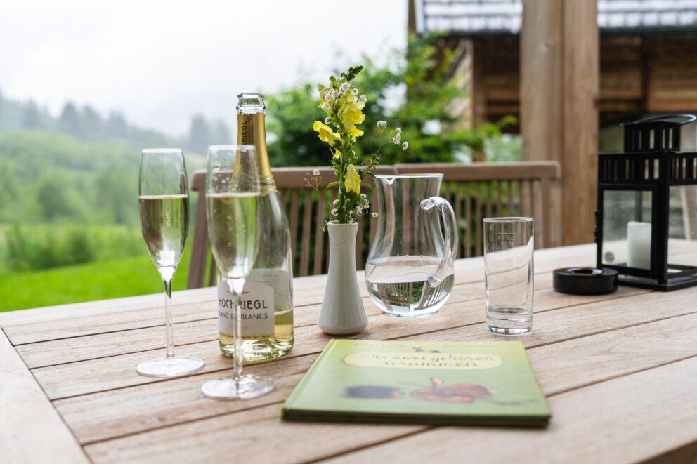 Tisch mit Sektflaschen und Gläsern vor grüner Landschaft auf Terrasse.