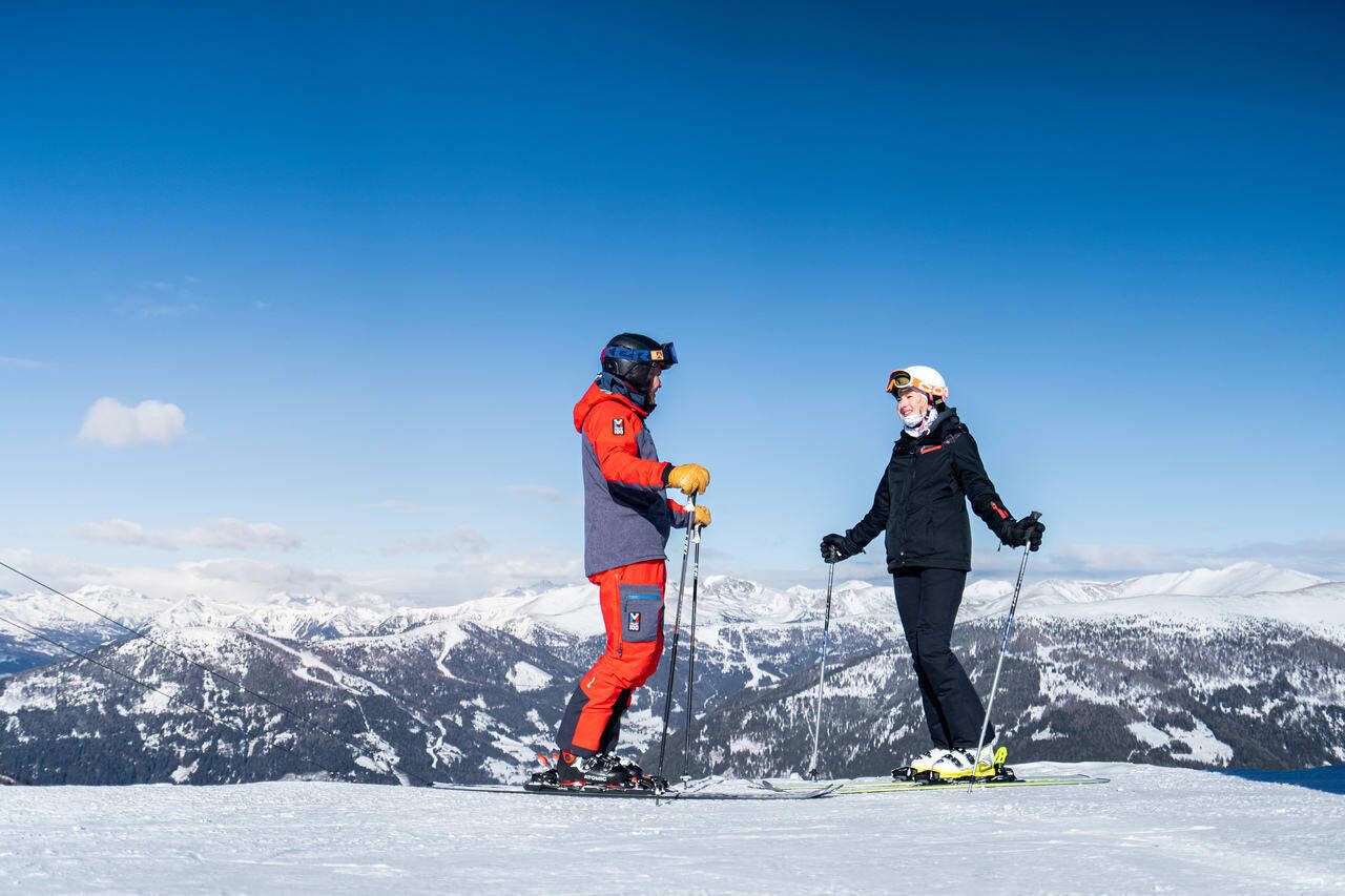 Zwei Skifahrer auf schneebedecktem Berg mit atemberaubender Aussicht auf die Nockberge.