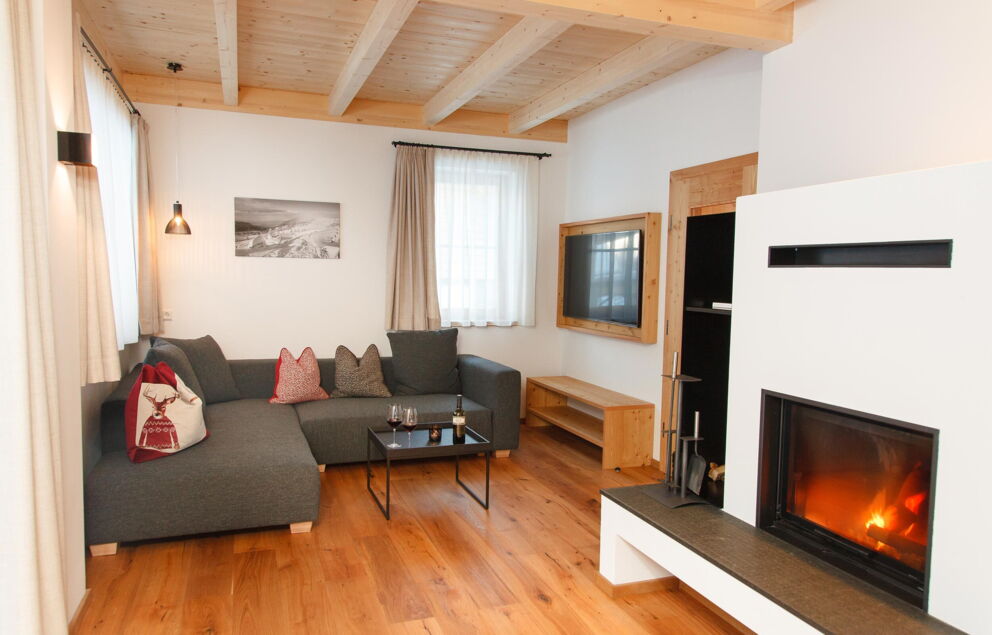 Wohnzimmer mit Kamin, grauem Sofa, Holzboden und warmem Licht.