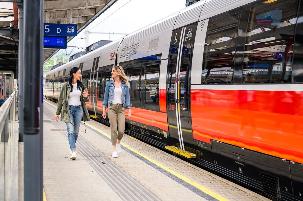 Zwei Frauen gehen am Bahnsteig neben einem modernen Zug entlang.