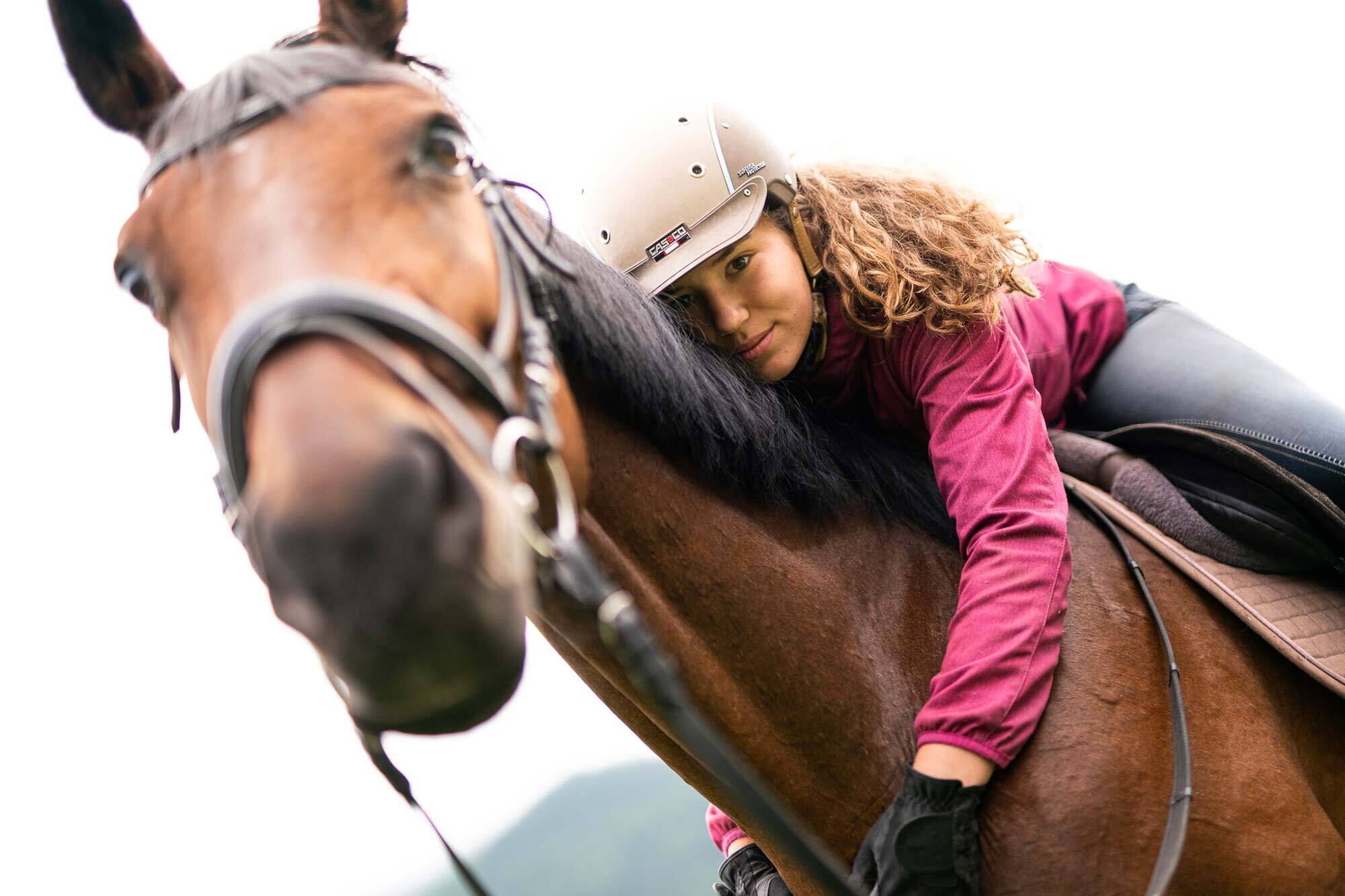 Woman in riding clothes embraces brown horse, radiant connection and trust.