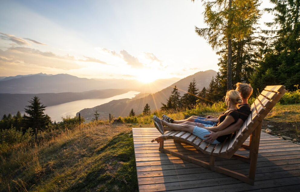 Paar auf Holzbank genießt Sonnenuntergang mit Berg- und Seeblick.