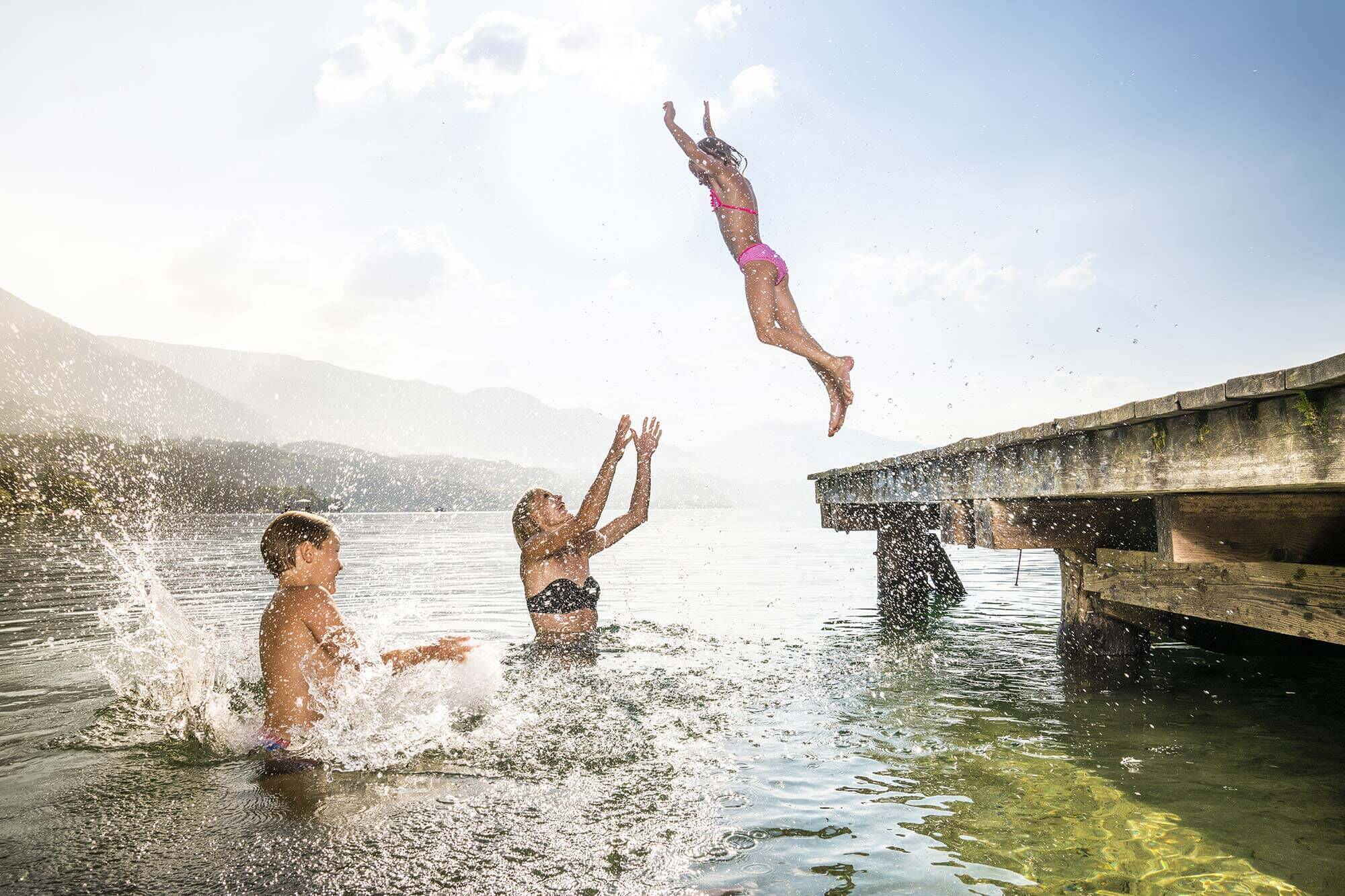 Kinder spielen im sonnigen Wasser neben einem Holzsteg.
