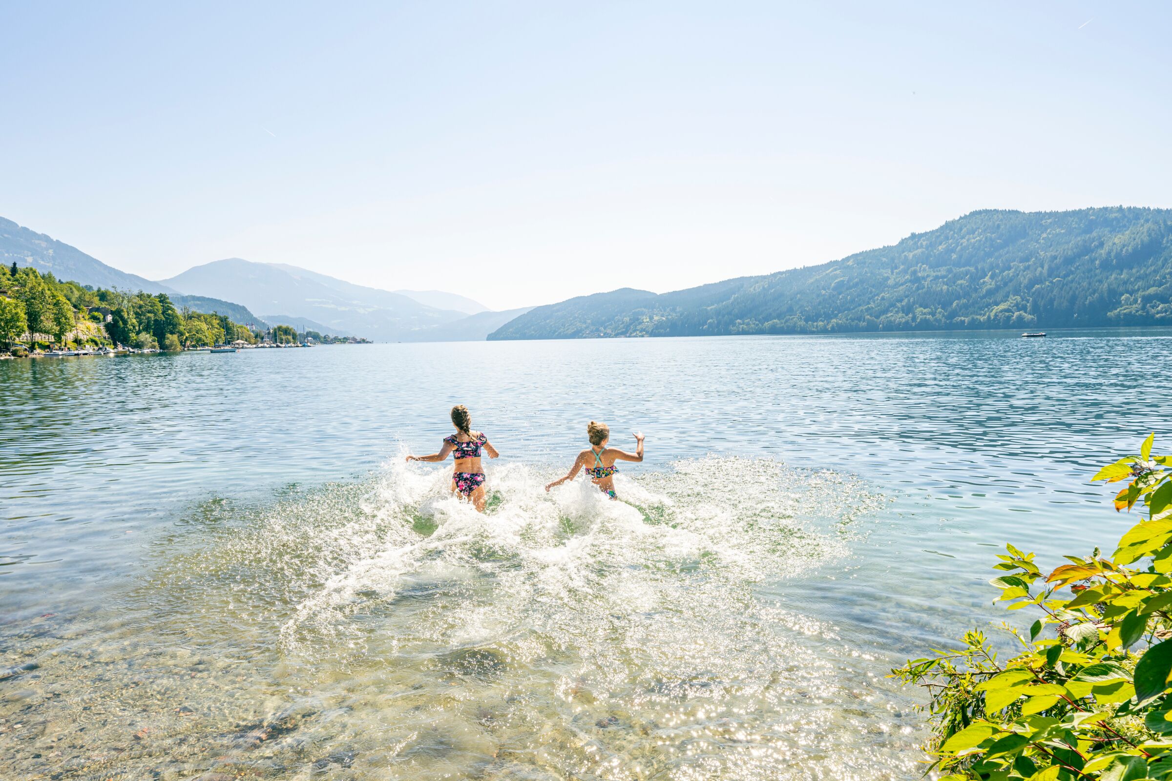 Due bambini che giocano in un lago limpido con le montagne sullo sfondo.