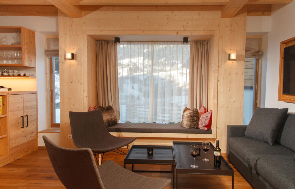 Gemütliche Sitzecke aus Holz mit Ausblick durch großes Fenster auf verschneite Landschaft.