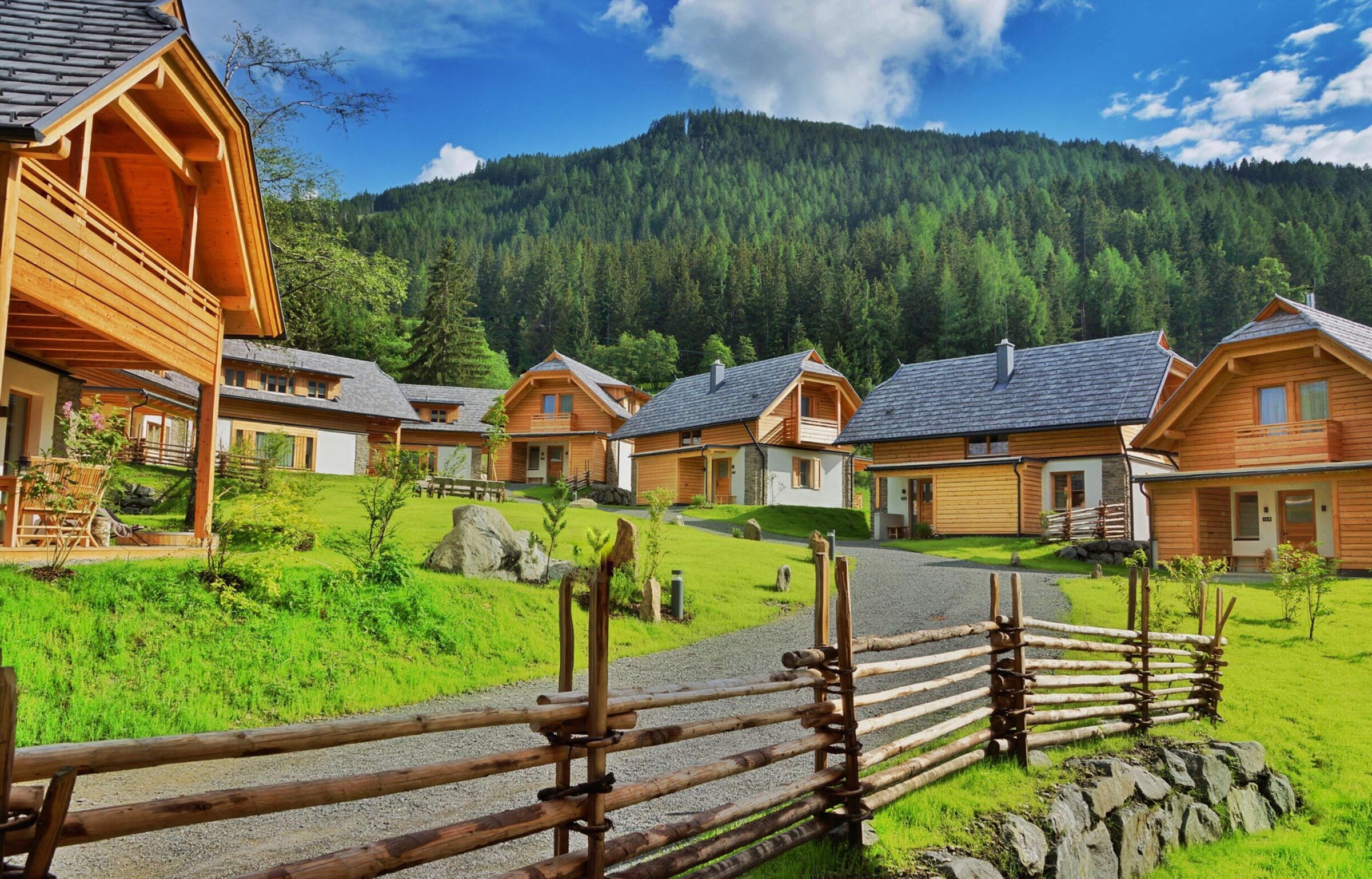 Gemütliche Chalets aus Holz in einer grünen Berglandschaft bei sonnigem Wetter.