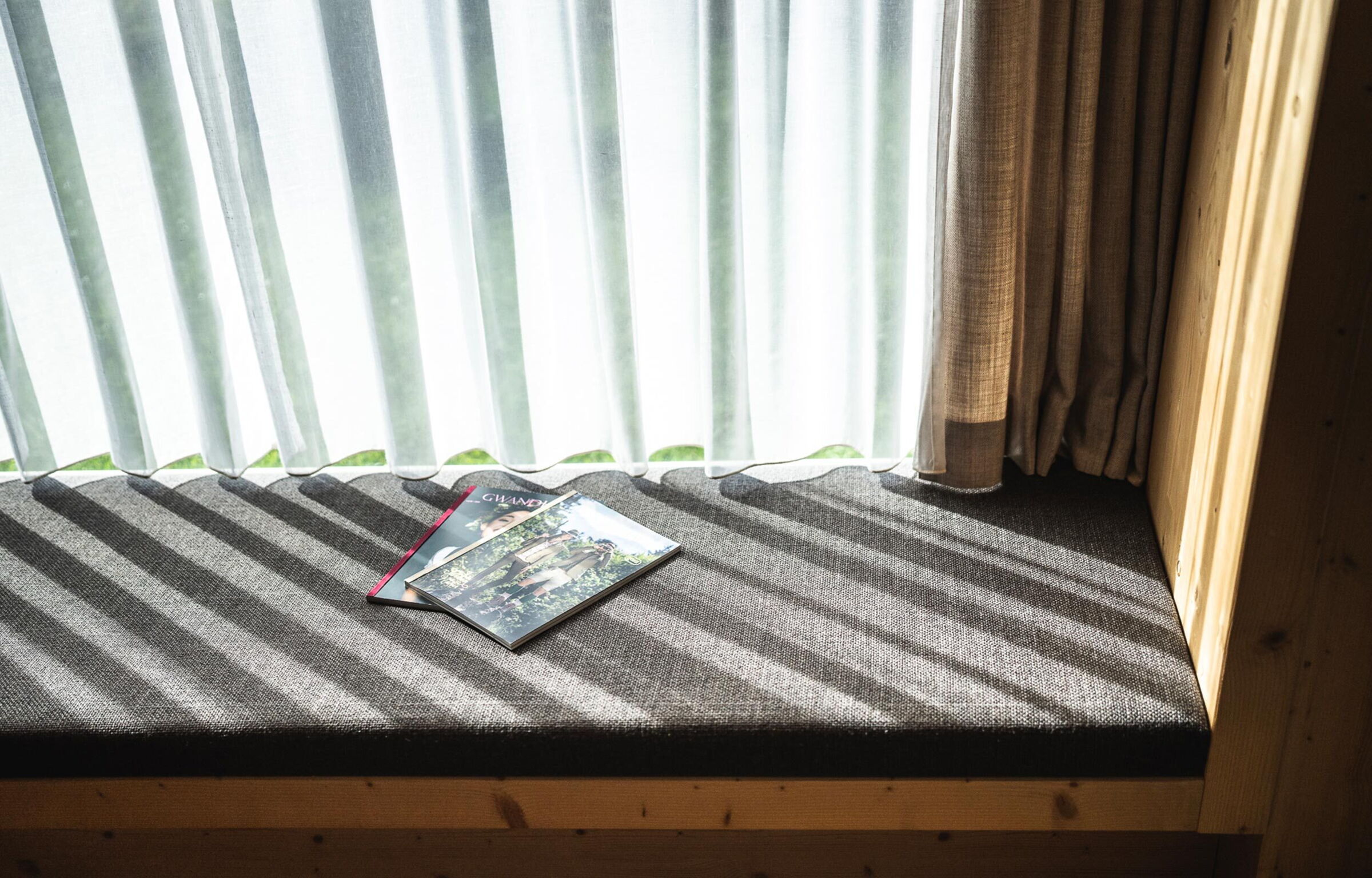 Gemütliche Sitzbank mit Buch neben lichtdurchfluteten Vorhängen in warmem Sonnenlicht.