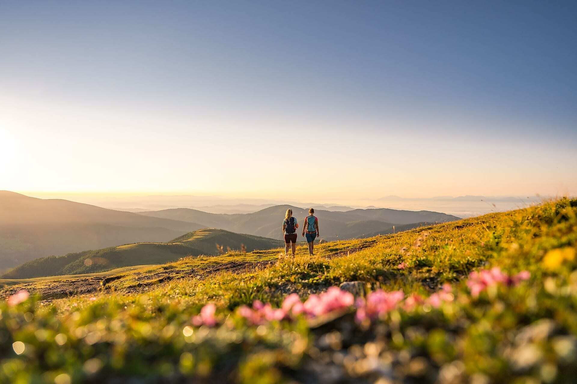 Zwei Wanderer genießen den Sonnenaufgang in den malerischen Nockbergen.