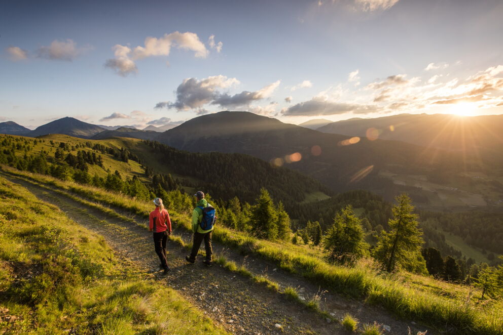 Zwei Wanderer genießen den Sonnenuntergang in den sanften Hügeln der Nockberge.