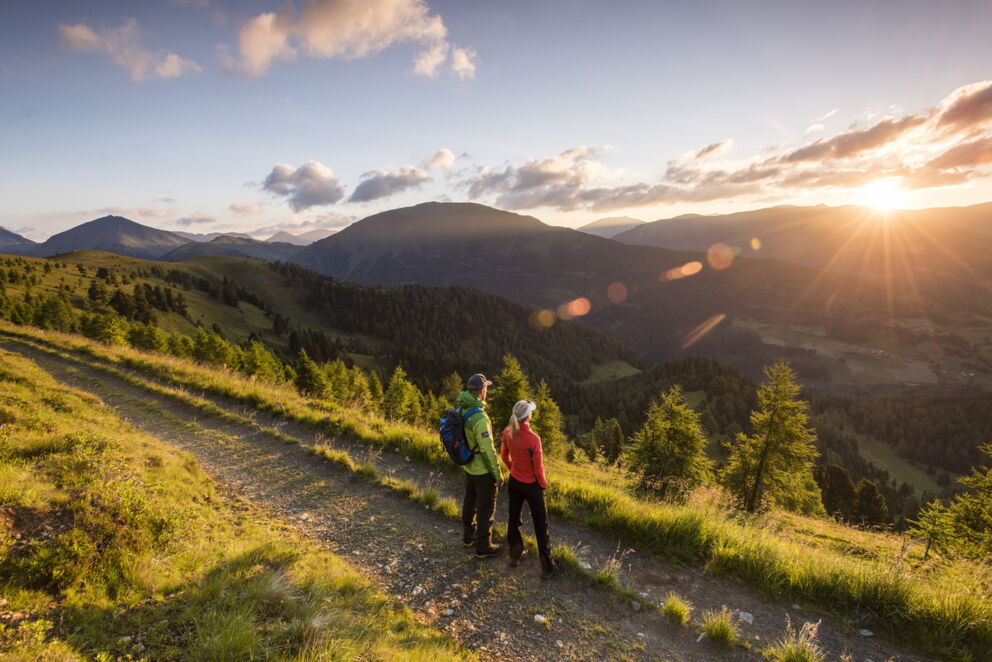 Zwei Wanderer genießen atemberaubenden Sonnenuntergang über den sanften Hügeln der Nockberge.
