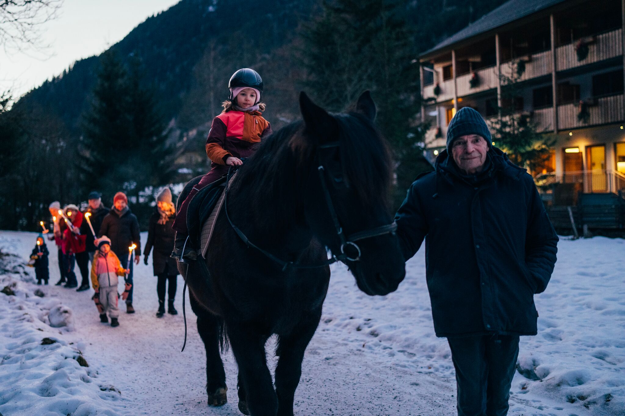 A group of people enjoy a torchlight walk with a horse in the snow.