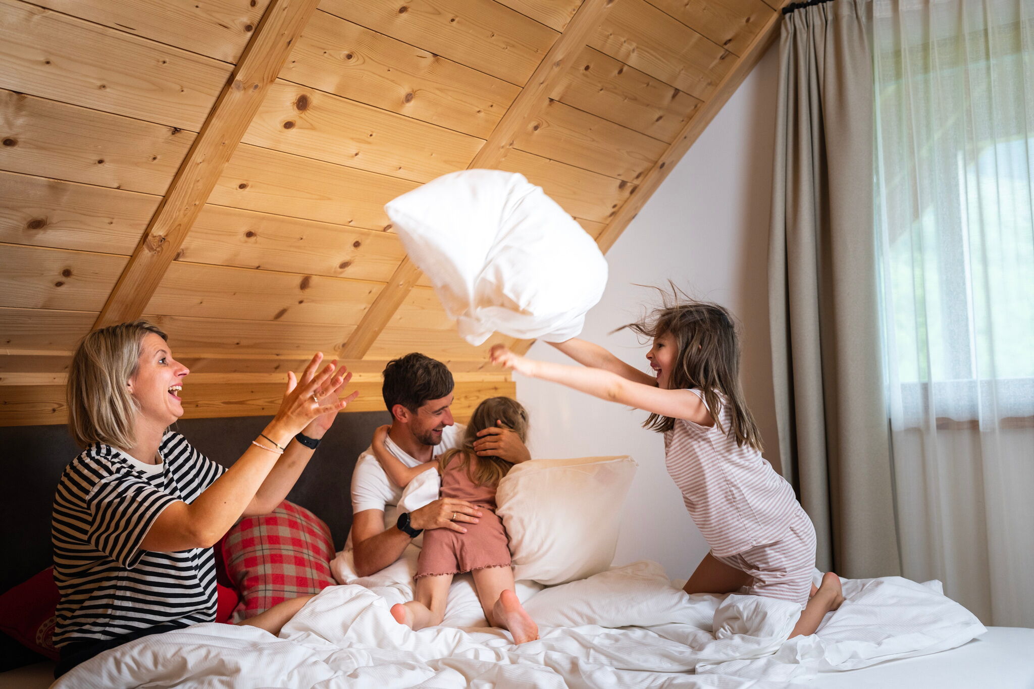 Familie spielt fröhlich auf einem Bett in einem gemütlichen Holzchalet.