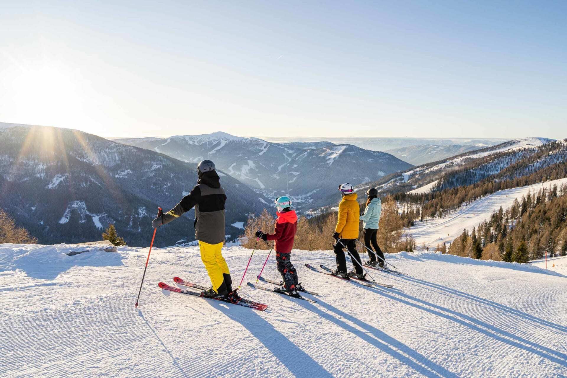 Familiengruppe auf Skipiste mit atemberaubender Berglandschaft im Sonnenlicht.