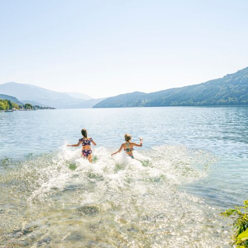 Due bambini che giocano in un lago limpido con le montagne sullo sfondo.