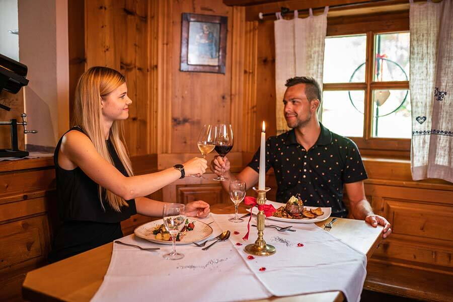 Couple toasting with wine, cozy wood paneling, candlelight, decorated table.