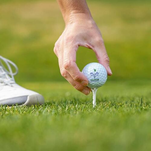 Hand platziert Golfball auf Tee auf grünem Rasen im Sonnenschein.