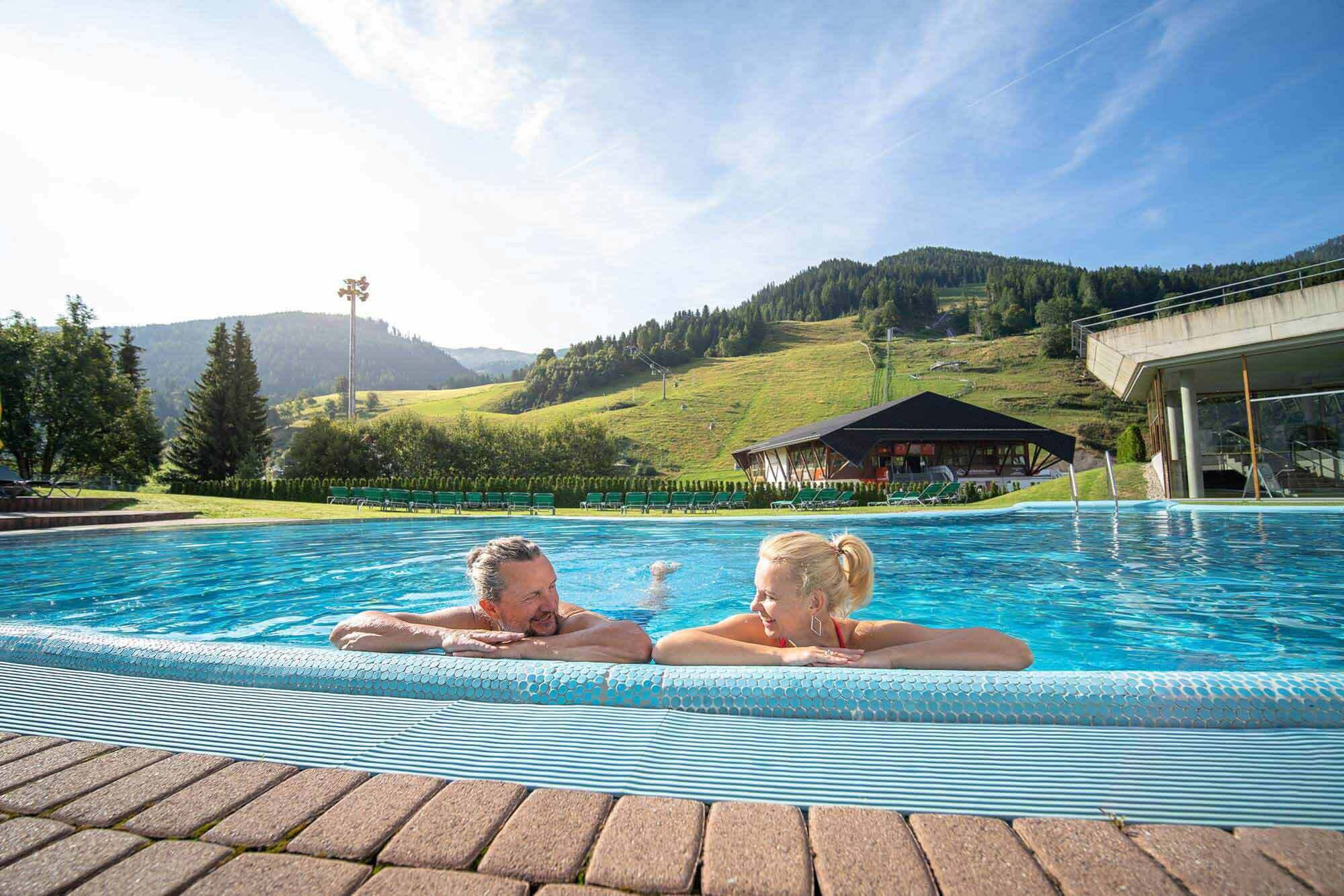 Two people relax in the pool with a wonderful view of the green mountains.