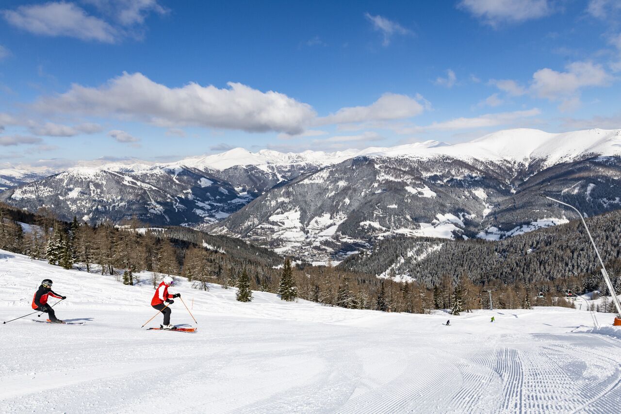 Two skiers on a snow-covered slope with a picturesque mountain panorama.