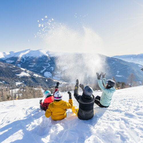 Familie spielt im Schnee mit Bergblick unter strahlender Wintersonne.