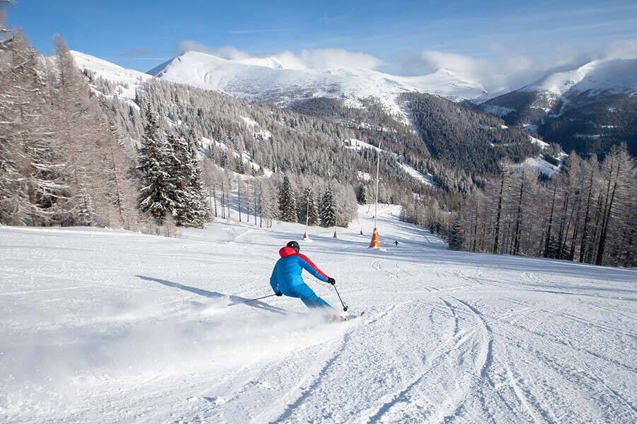 Skiers on a snow-covered slope, surrounded by snow-covered mountains and forests.