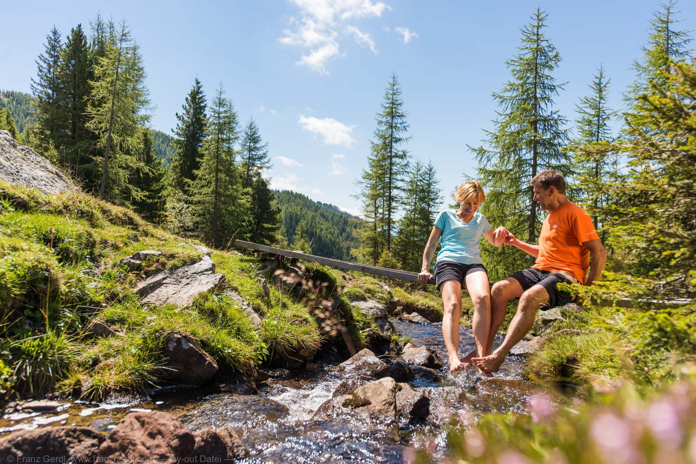 Paar genießt barfuß einen Bach in den sonnigen Kärntner Nockbergen.