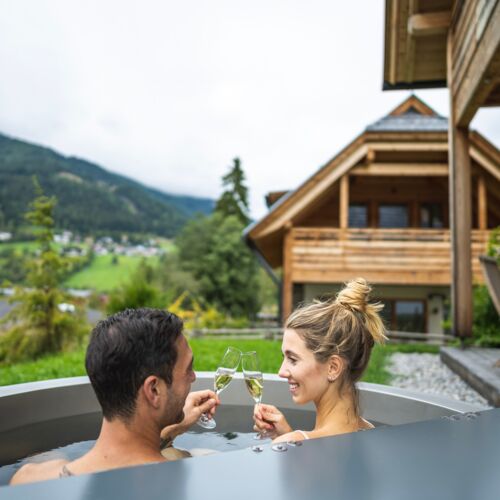 Couple relaxing in the whirlpool with champagne, surrounded by alpine scenery and chalets.