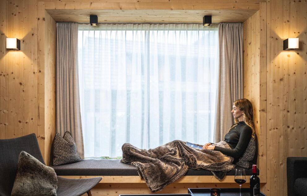 Frau entspannt in gemütlicher Fensternische mit Kissen und Decke aus Naturmaterialien.