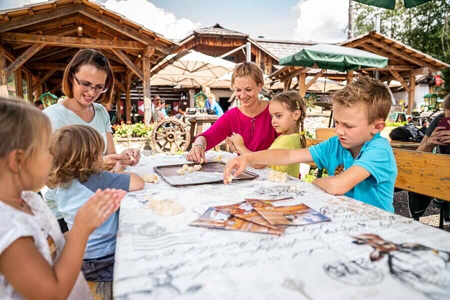 Molti bambini si siedono con due assistenti su una panchina accanto alla fattoria dei pony in Carinzia e giocano