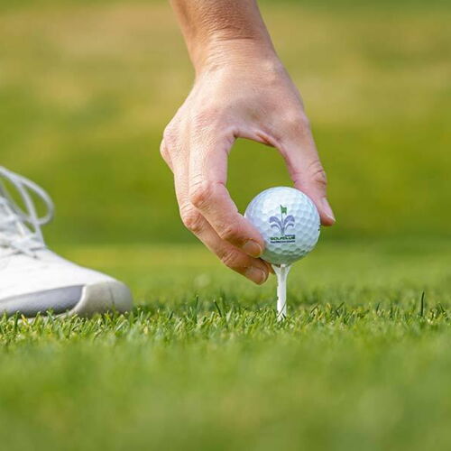 Hand platziert Golfball auf Tee auf grünem Rasen im Sonnenschein.