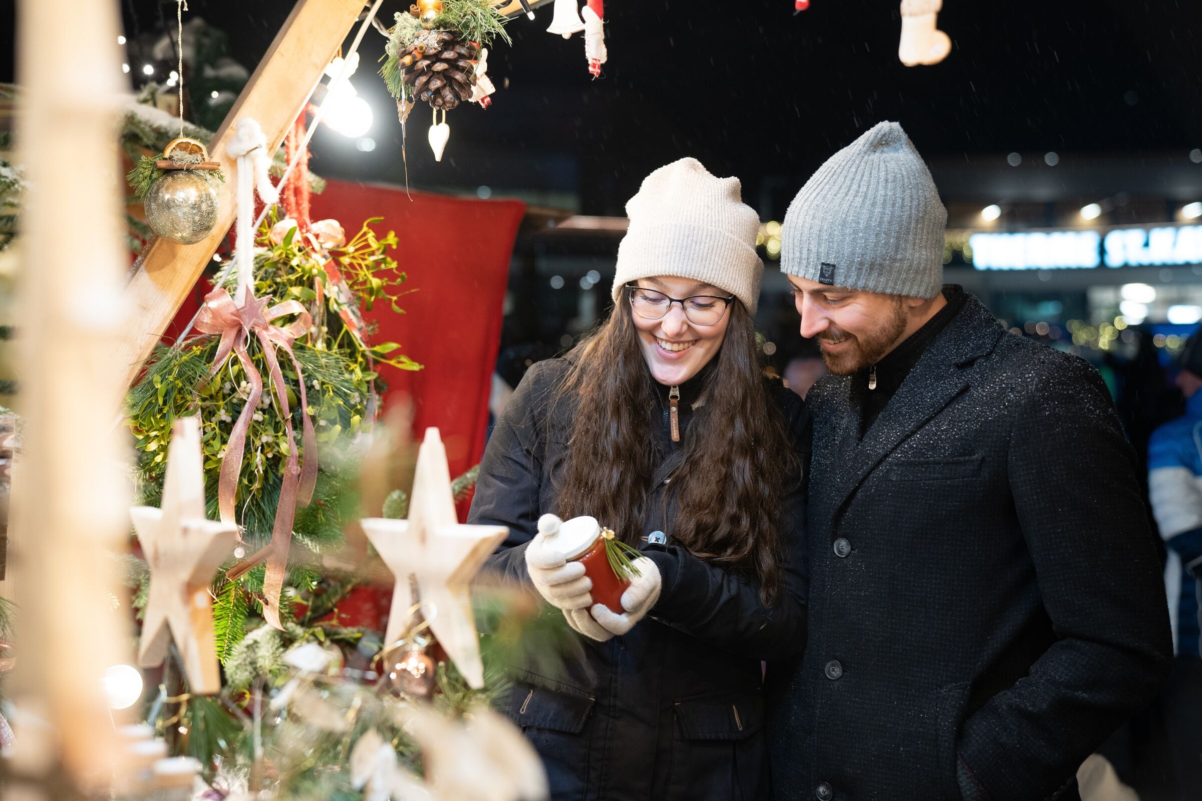 Smiling couple exploring an outdoor market stall decorated for Christmas.