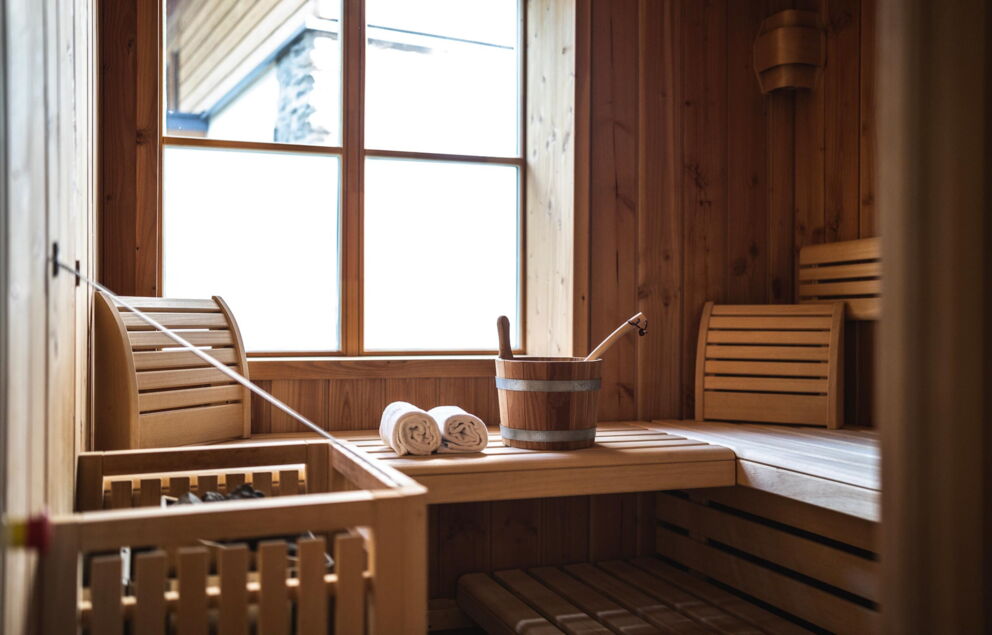 Holzsauna mit Fenster, zwei Handtücher und Saunaeimer auf der Bank.