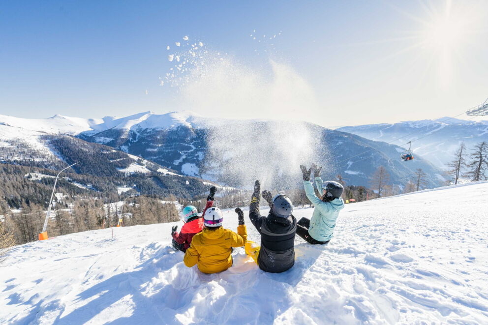 Family playing in the snow with a mountain view under a bright winter sun.