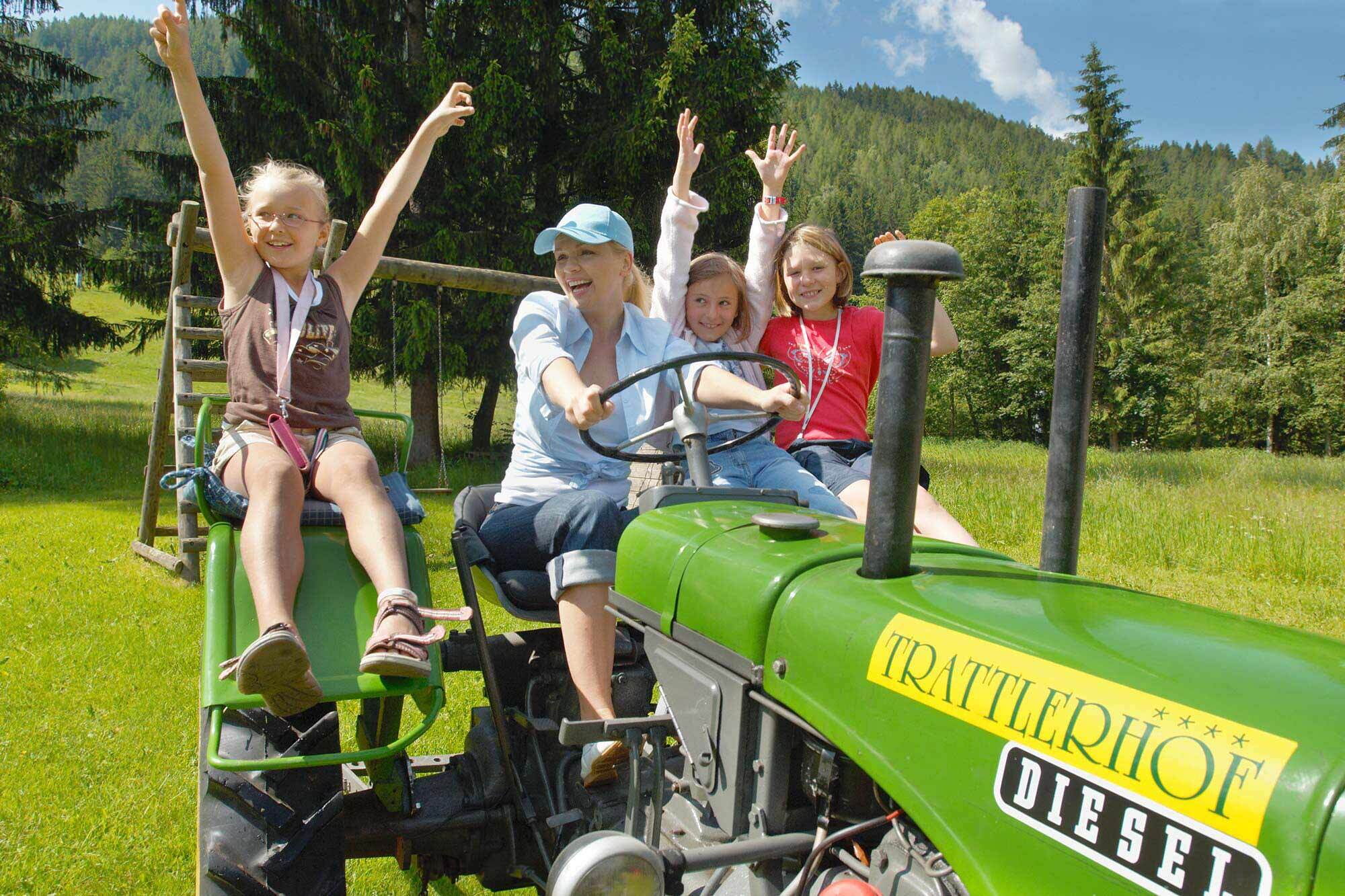 Familie auf grünem Traktor, lachend und mit erhobenen Armen in der Natur.