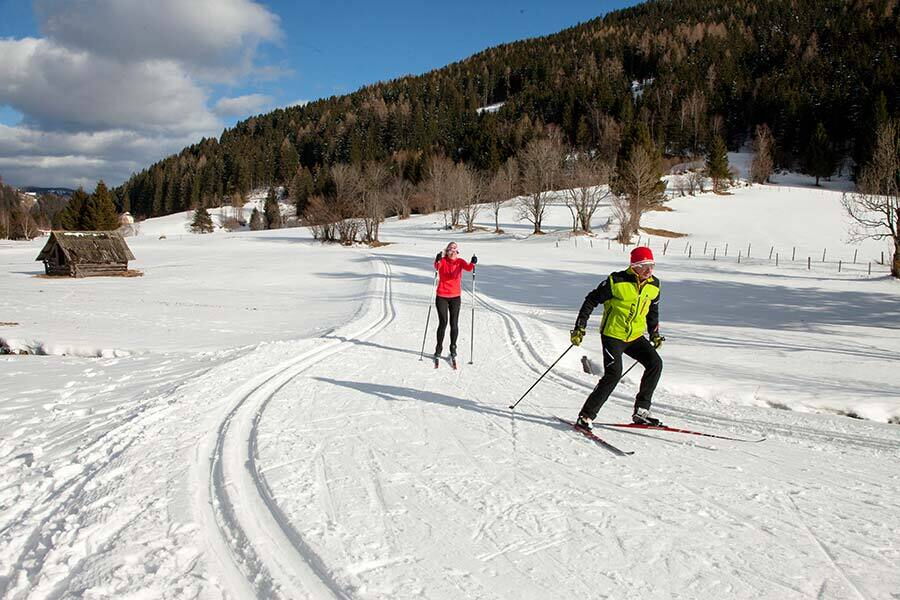 Two people cross-country skiing against a snow-covered mountain backdrop in Carinthia.