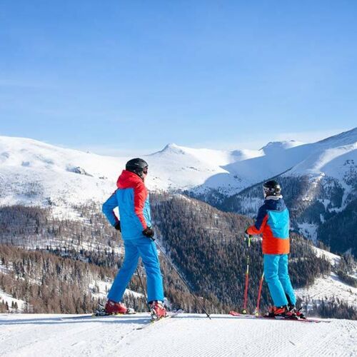 Vater und Sohn stehen in Skiausrüstung auf einer Piste und bestaunen die Natur in Kärnten