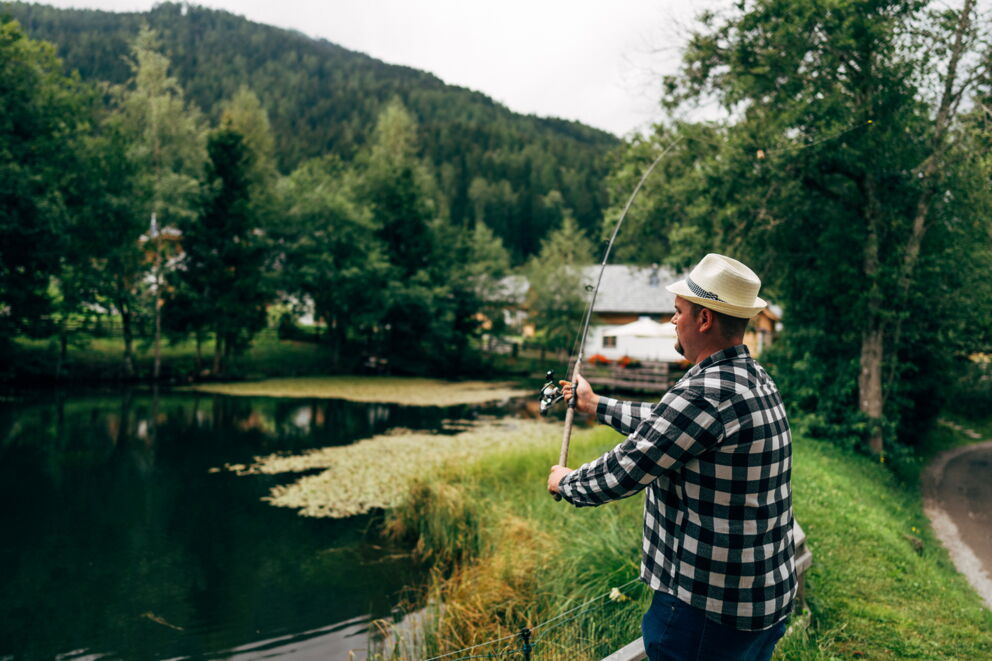 Mann angelt am ruhigen Waldteich in idyllischer Berglandschaft.
