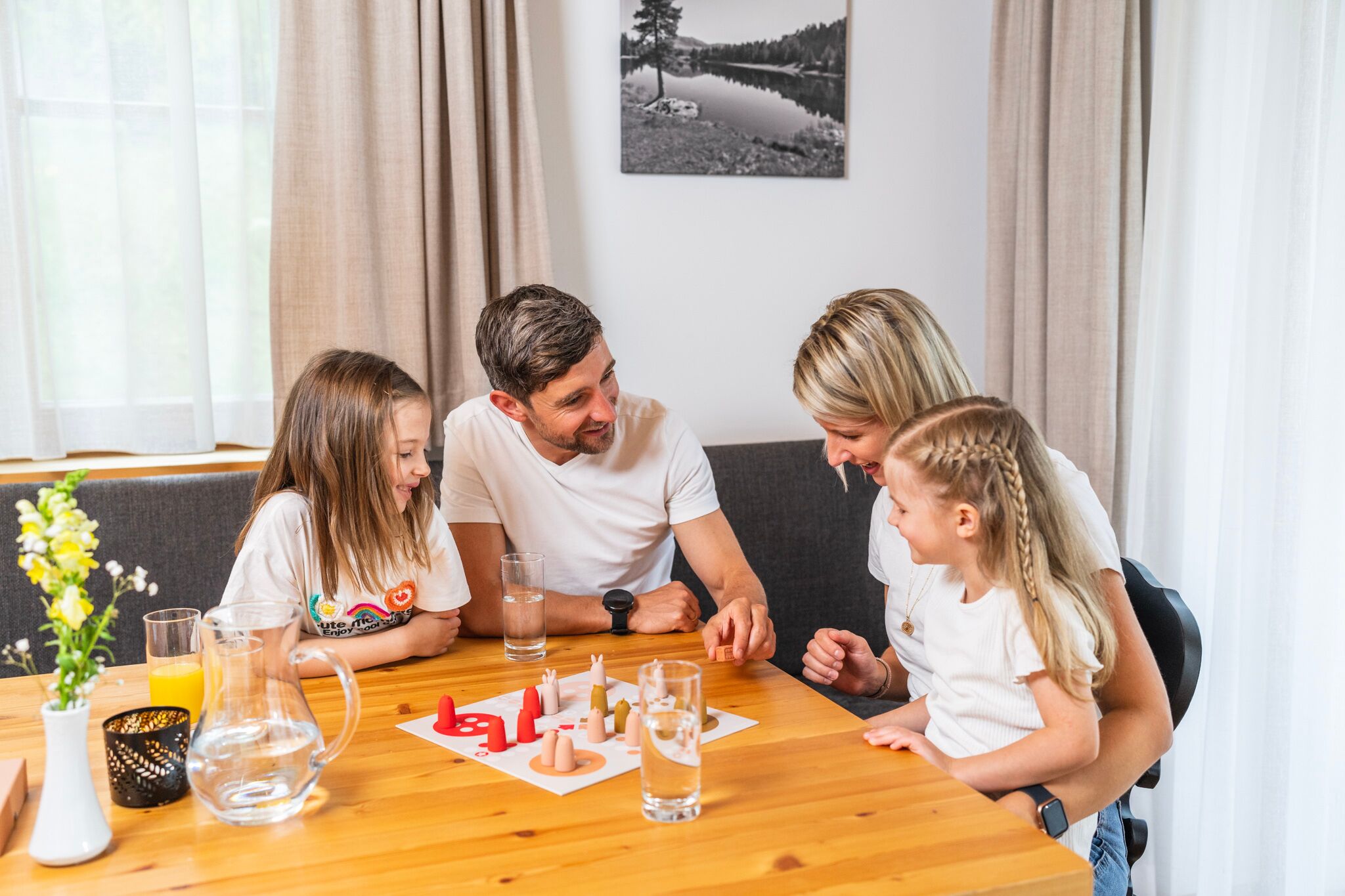 Familie spielt fröhlich ein Brettspiel am Holztisch in gemütlicher Chalet-Atmosphäre.