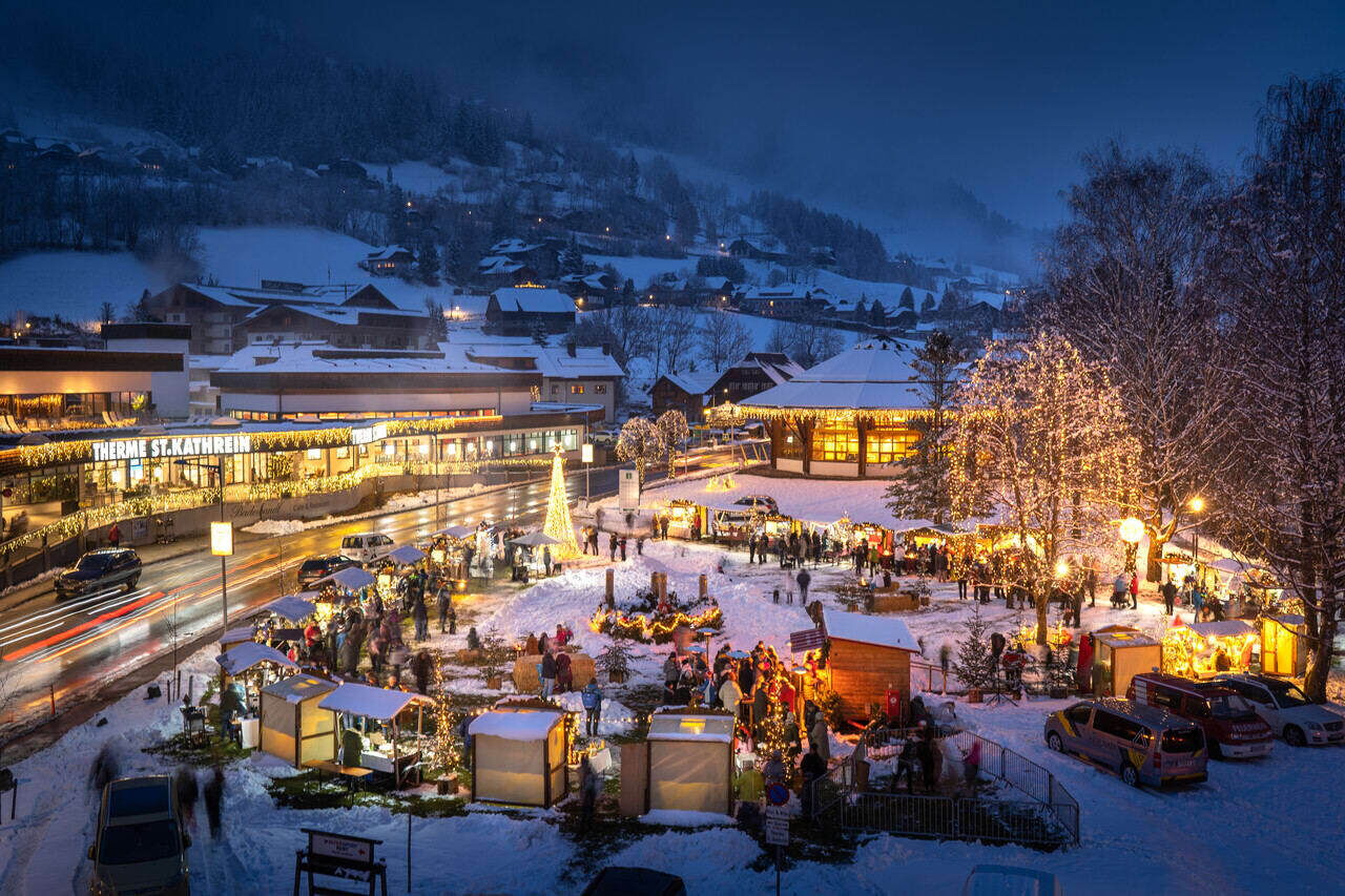 Festively illuminated Christmas market with a snow-covered village in the background, atmospheric and inviting.