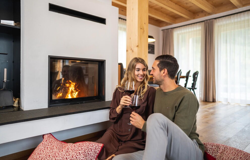 Couple enjoying wine in front of a crackling fireplace in the cozy chalet.