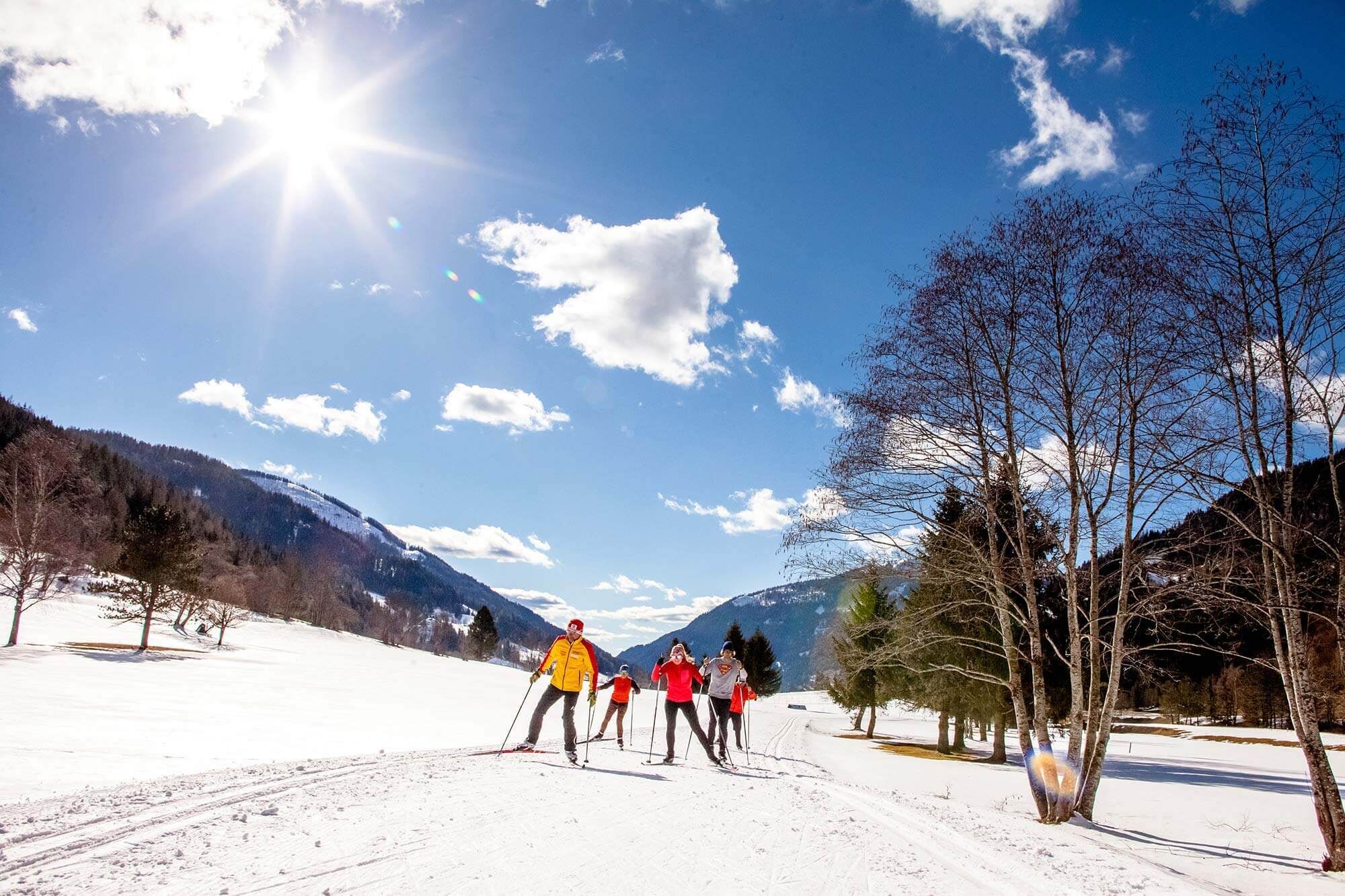 Group of cross-country skiers in a sunny, snow-covered mountain landscape under a blue sky.