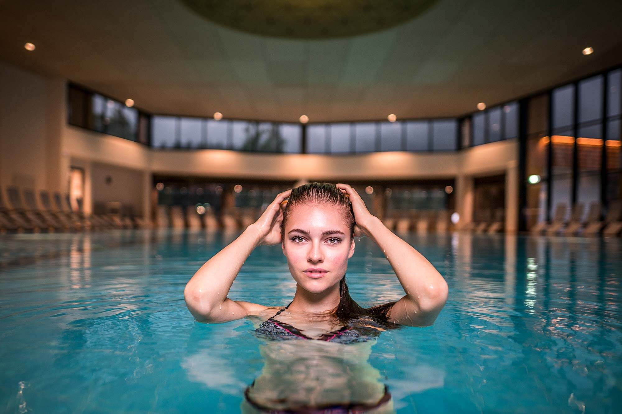 Frau genießt erfrischendes Bad im modernen, lichtdurchfluteten Indoor-Pool.