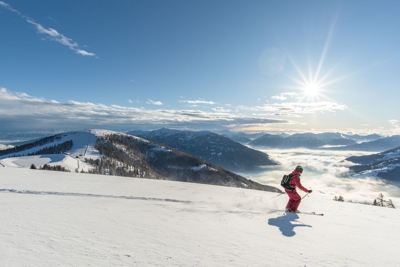 Skifahrer auf verschneitem Berg mit strahlendem Sonnenschein und weitem Talblick.