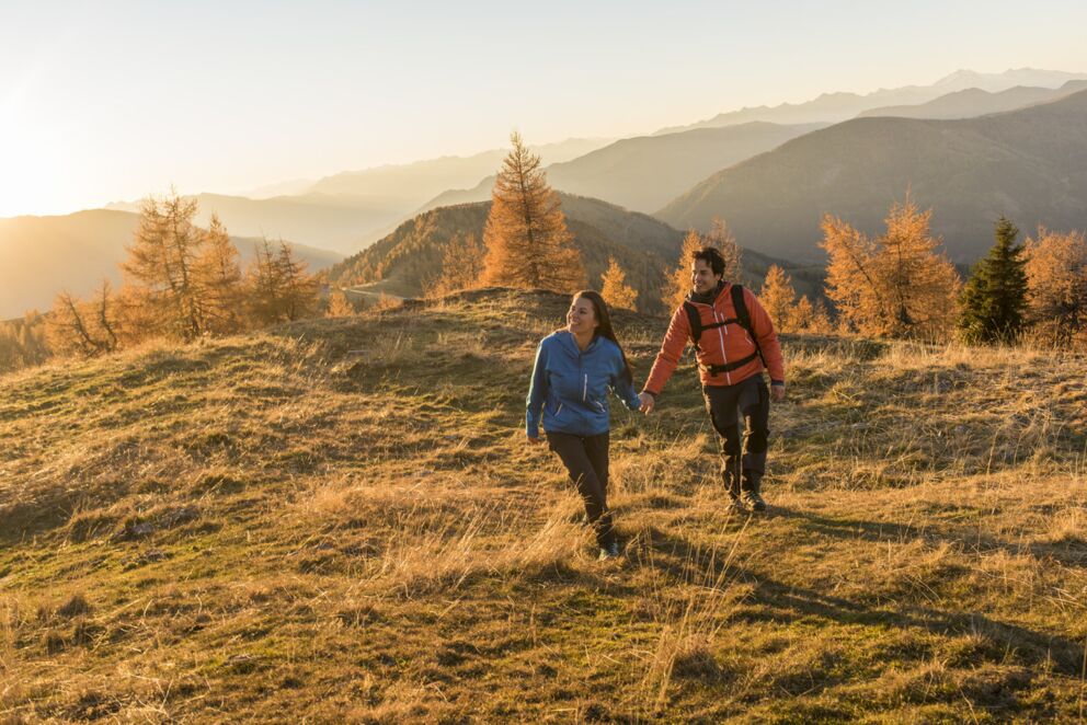 Paar wandert Hand in Hand durch goldene Herbstlandschaft der Nockberge.