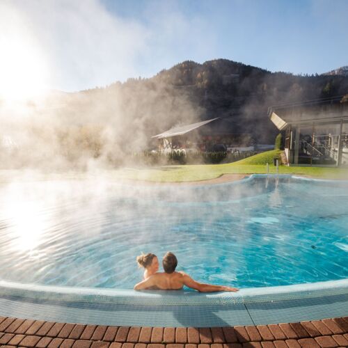 Paar genießt warmes Thermalwasser unter blauem Himmel mit Bergblick.