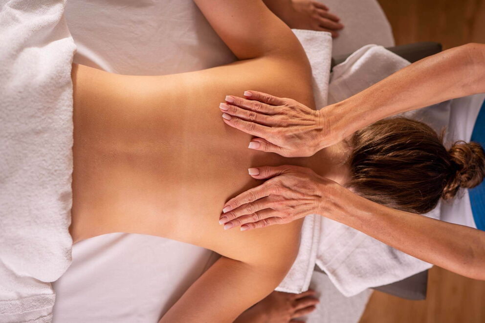Woman receives back massage on soft white towel for total relaxation.