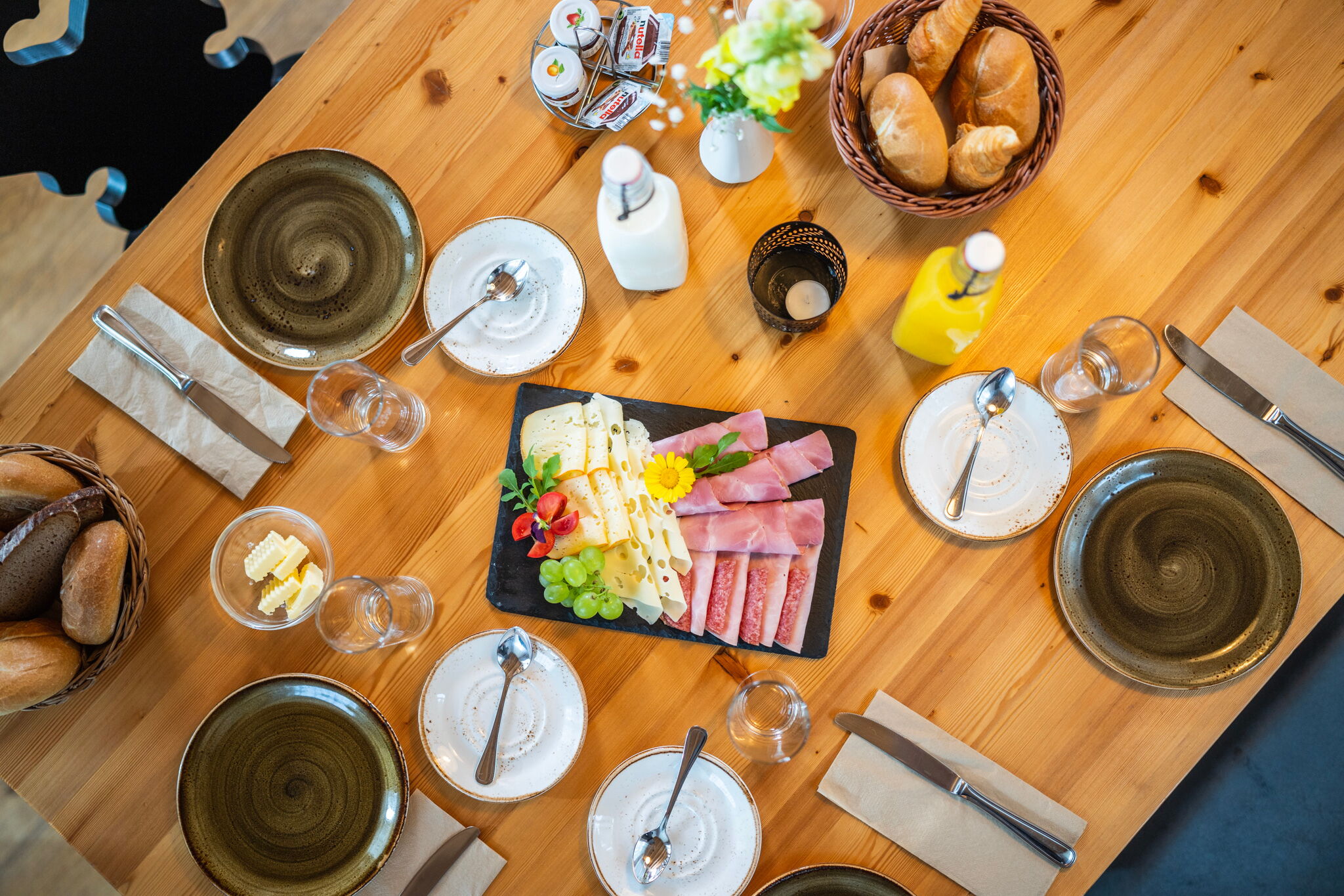 Tavola con salumi, formaggi, pane e bevande per una colazione abbondante.