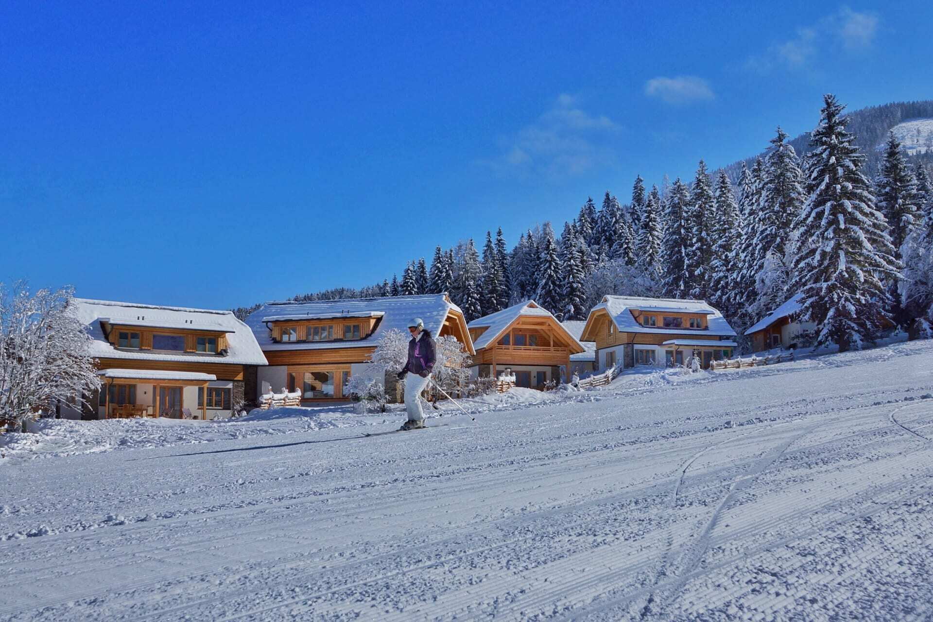 Chalet innevati in un pittoresco paesaggio invernale con cielo azzurro e sciatori.