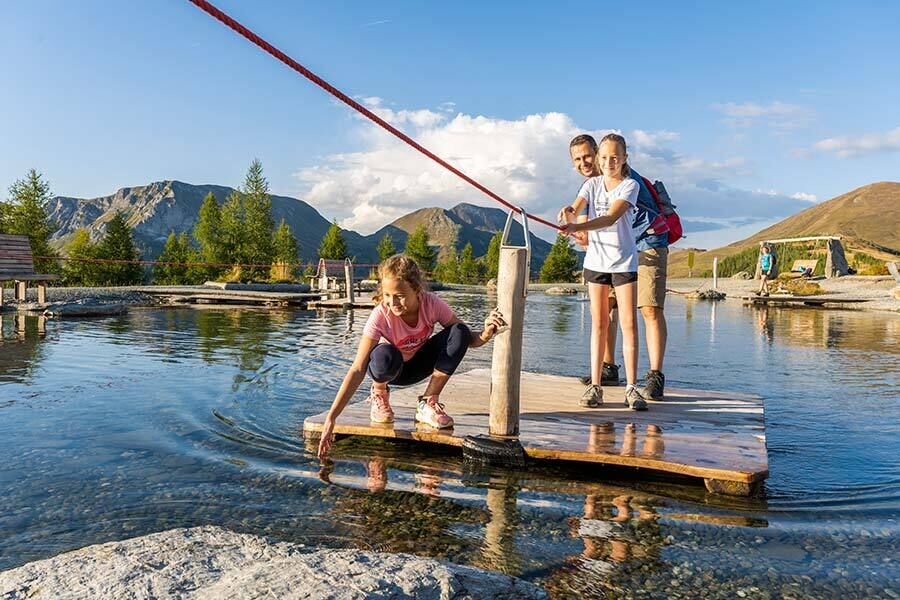 Family on a wooden raft enjoying a clear mountain lake with a magnificent mountain backdrop